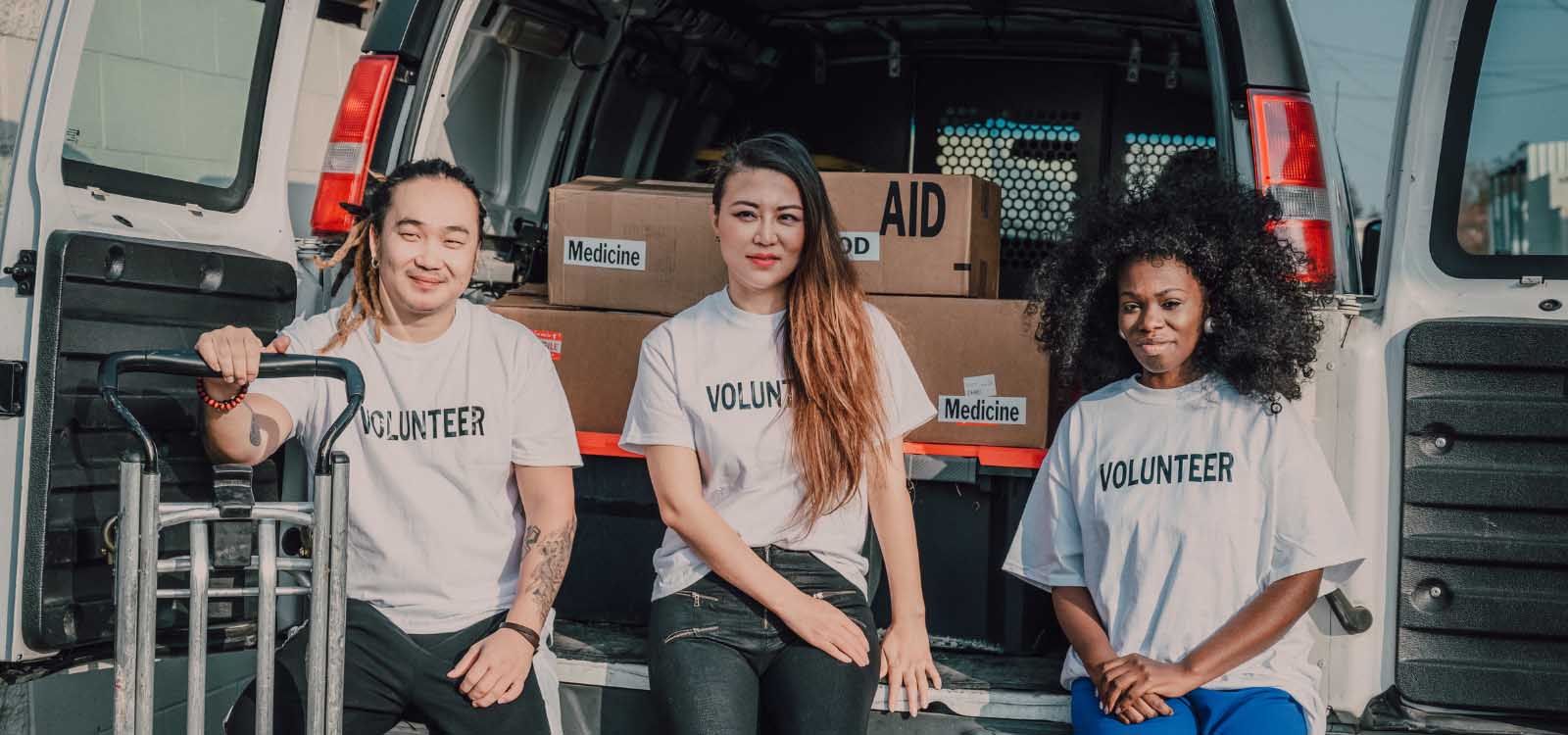 Three persons dressed in white shirts, positioned in the back of a van, appearing relaxed and social.